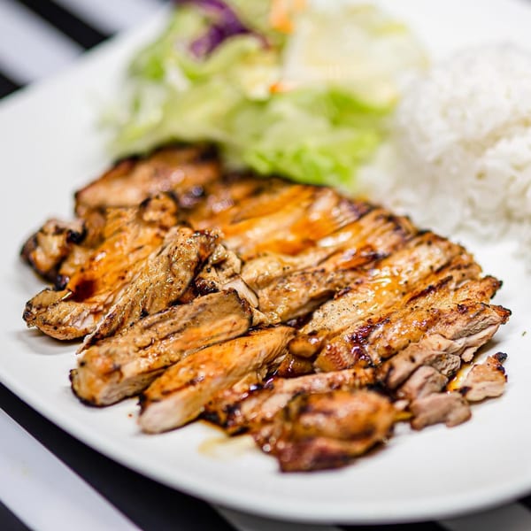 Grilled teriyaki chicken with a side of white rice and fresh green salad on a white plate.