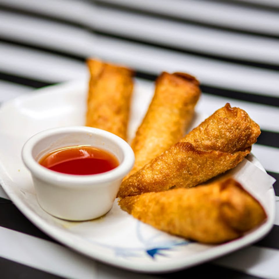 Four golden-brown egg rolls and a small white dish of red dipping sauce on a white plate.