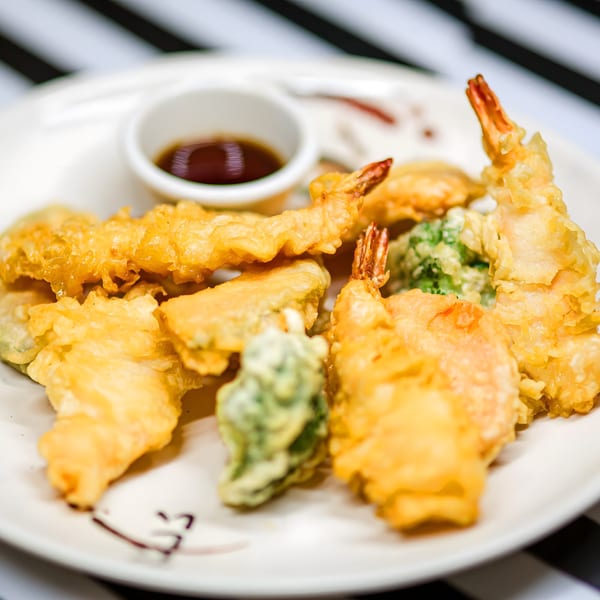 Crispy golden tempura shrimp and vegetables with a side of dipping sauce on a white plate.