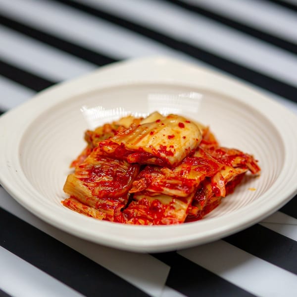 A white bowl filled with vibrant red kimchi, a traditional Korean side dish, on a striped surface.